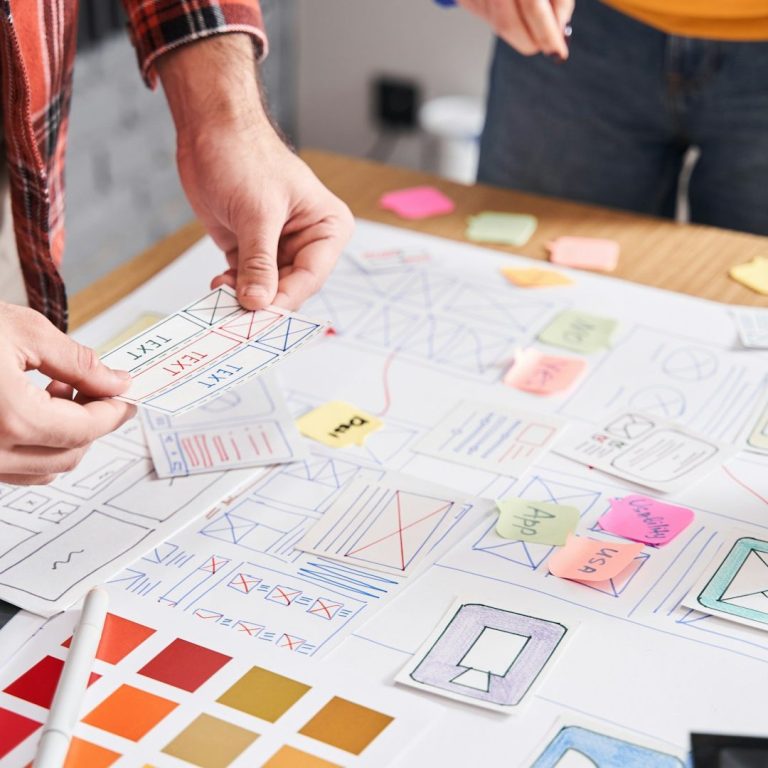 Hands working with sketches, colour swatches, and sticky notes on a design project.