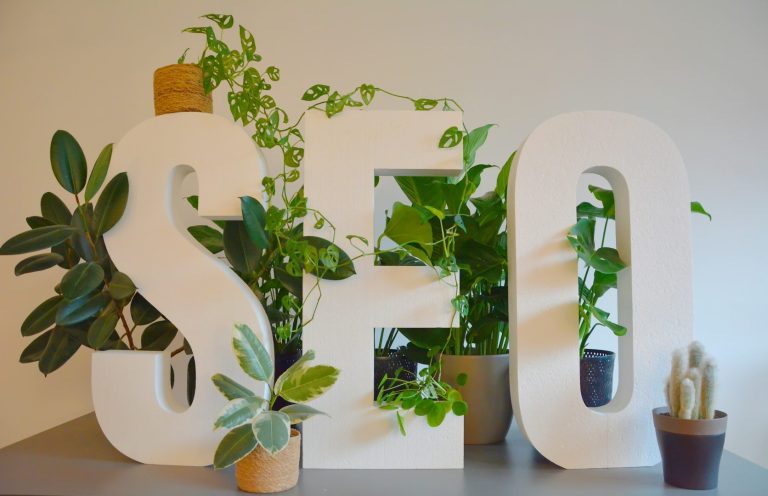 White letters spelling "SEO" surrounded by various green plants in pots.